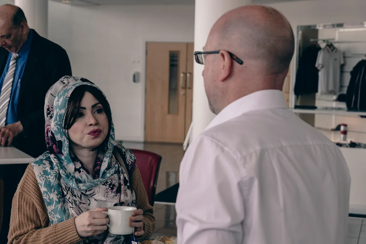 Two colleagues in conversation over coffee in a bright office foyer